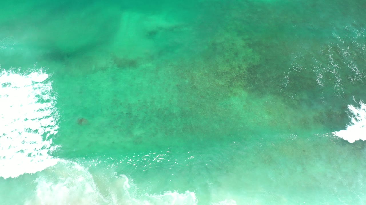 Top-down view of turquoise water in Los Cabos, Mexico, with white surf entering from the bottom edge and no visible people.