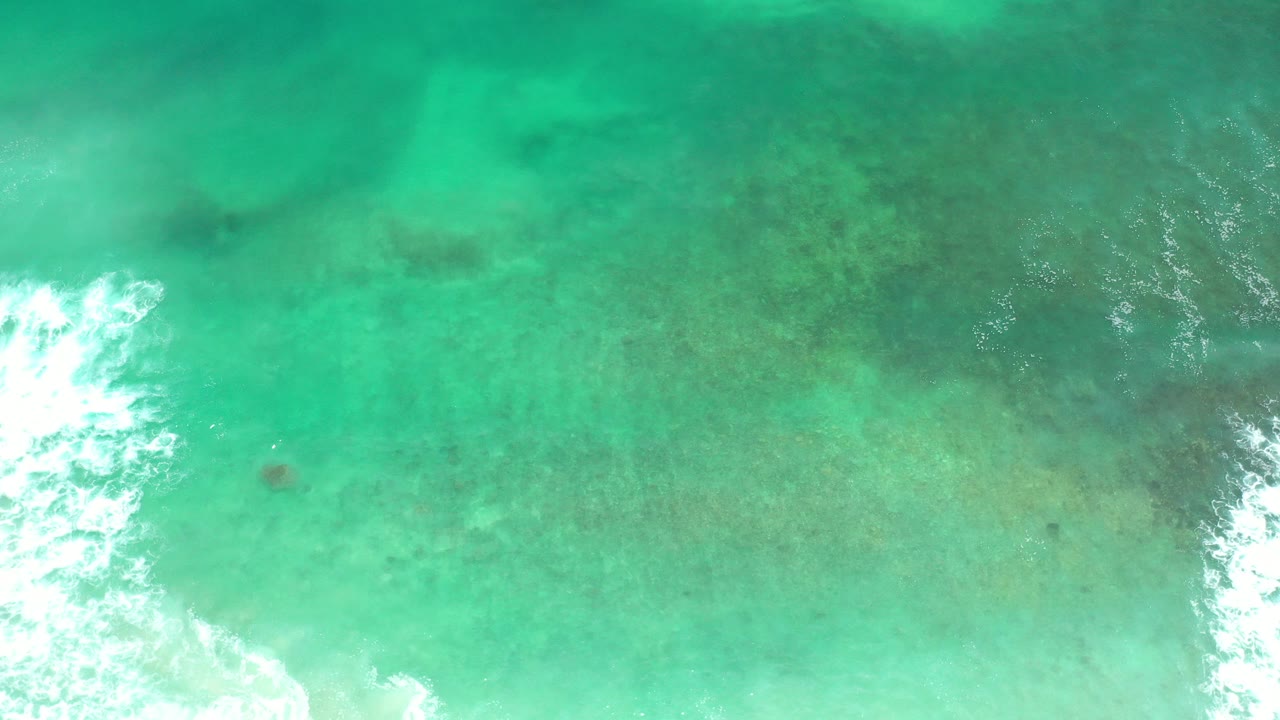 Overhead view of turquoise ocean water in Los Cabos, Mexico, with a bright white surf break entering from the lower left and no visible people.
