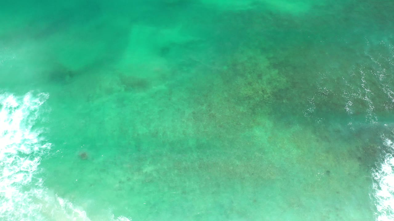 Turquoise ocean surface with darker underwater areas and white foam near the bottom.