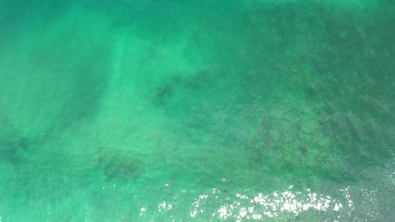 Overhead green blue ocean water with faint darker patches and sun glare near the lower edge.