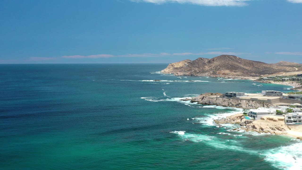 Ocean and rocky Los Cabos shore with surf lines and hills in the background.
