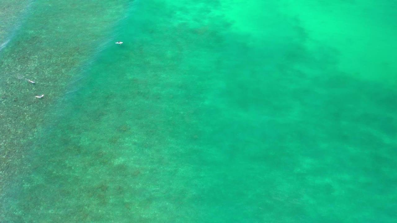 Turquoise water over reef with small white objects near left edge