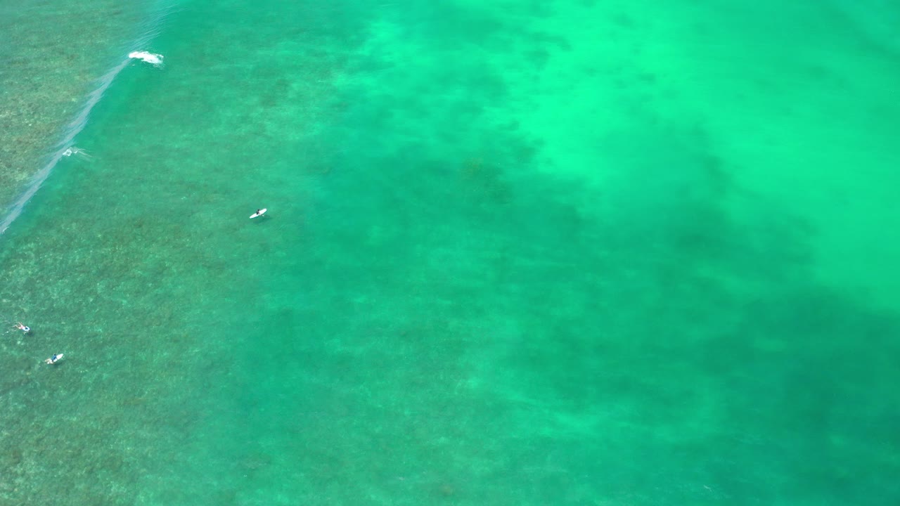 Overhead view of turquoise water in Los Cabos, Mexico, with darker reef texture on the left edge, small white wave breaks, and no visible people.