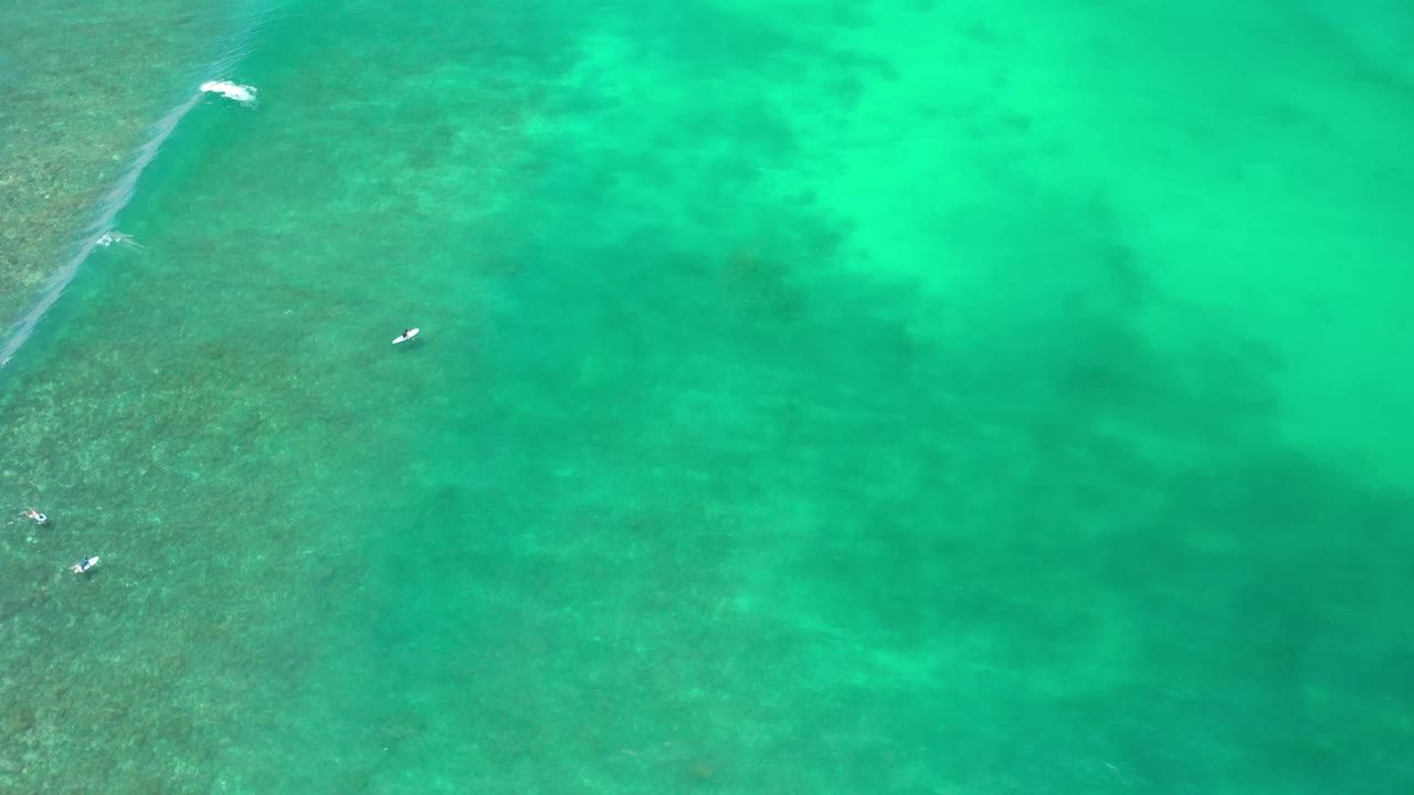 High overhead Los Cabos water view with green-blue ocean, darker submerged texture, small white marks near the left side, and no visible people.