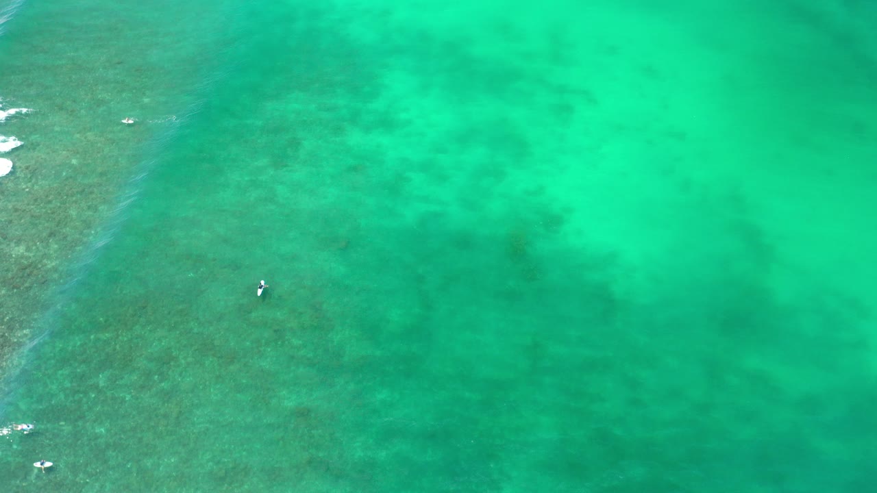Overhead frame from Los Cabos, Mexico showing turquoise ocean, darker reef patches at left, a small white boat near center-left, and no visible people.