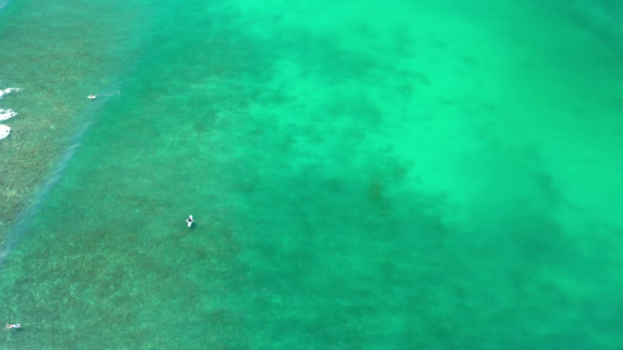 Aerial ocean frame with a small boat and breaking water at left.