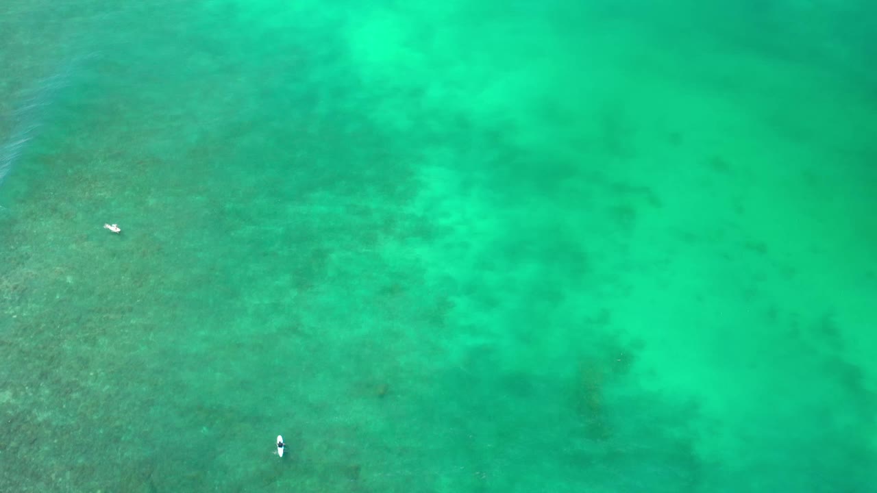 Aerial view of green-blue Los Cabos water with mottled darker seabed areas, a small pale object near the lower center, and no visible people.