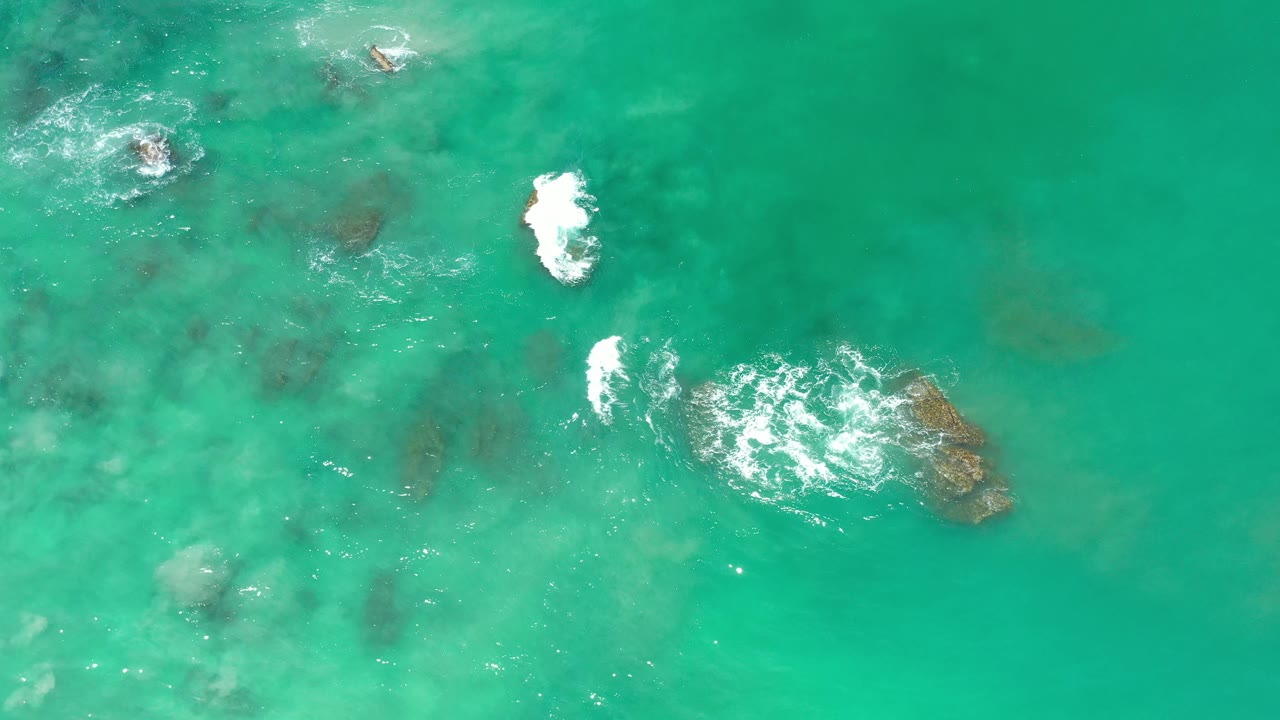 White surf marks two rock areas in turquoise water.