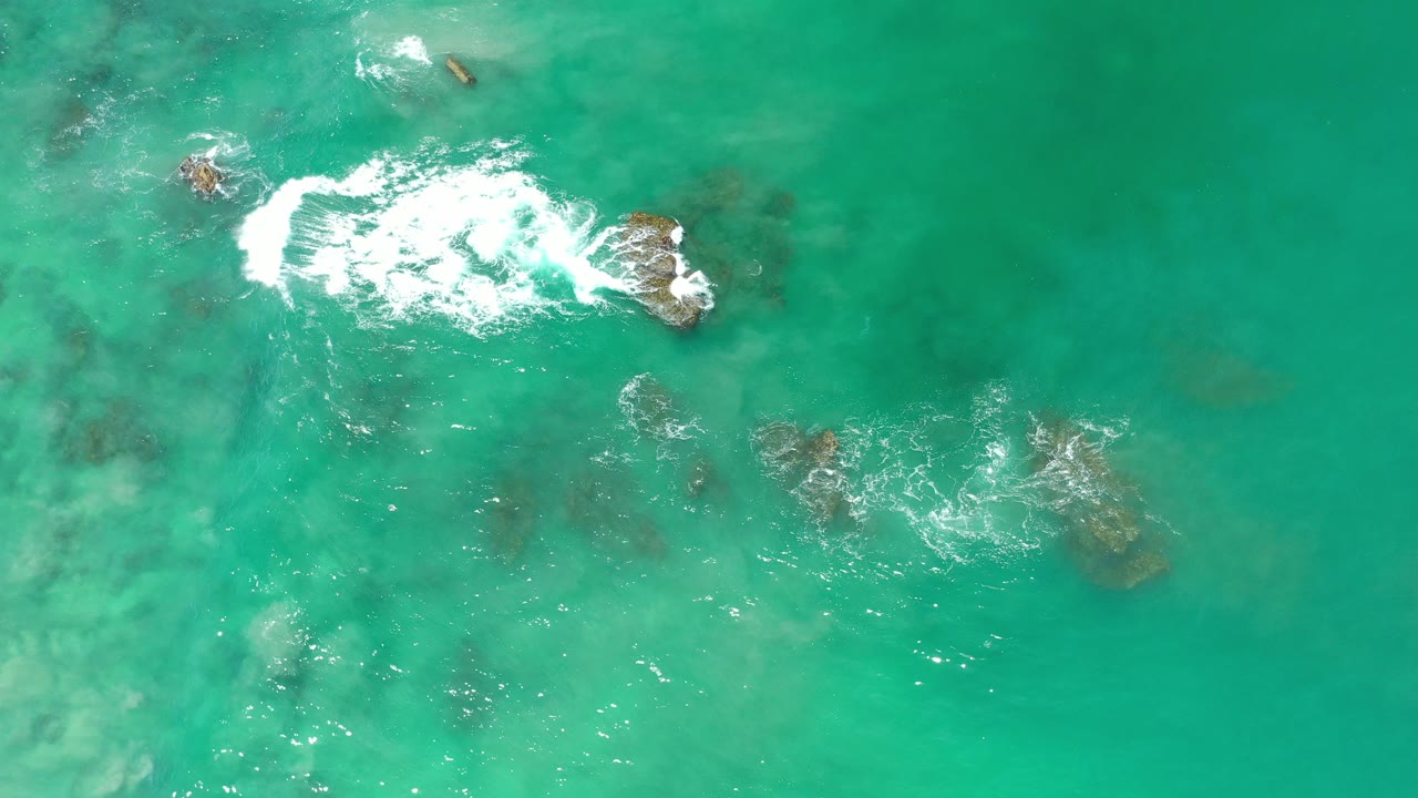 Overhead turquoise water with waves breaking over dark rocks.