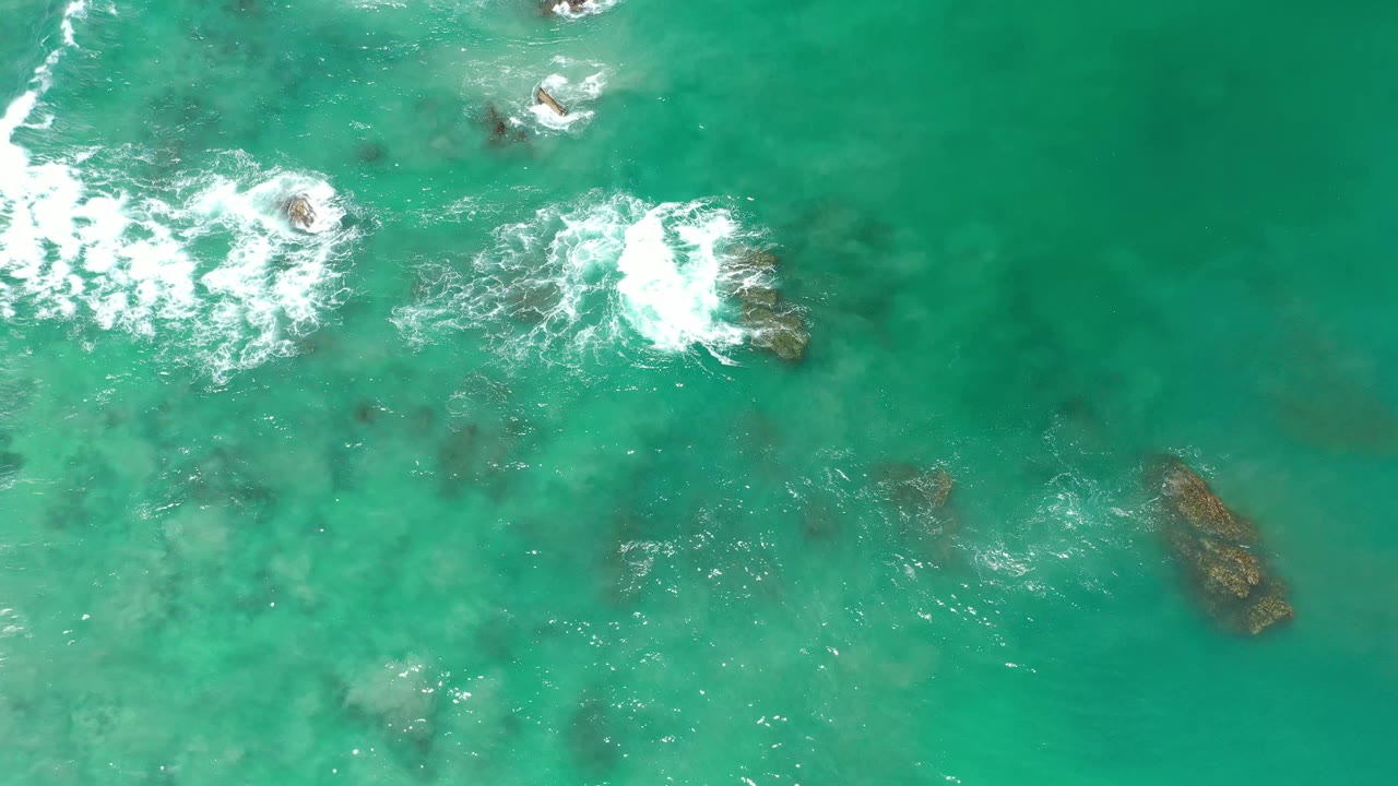 Aerial frame from Los Cabos, Mexico, showing foamy surf hitting shallow reef patches in clear green-blue water, no visible people.