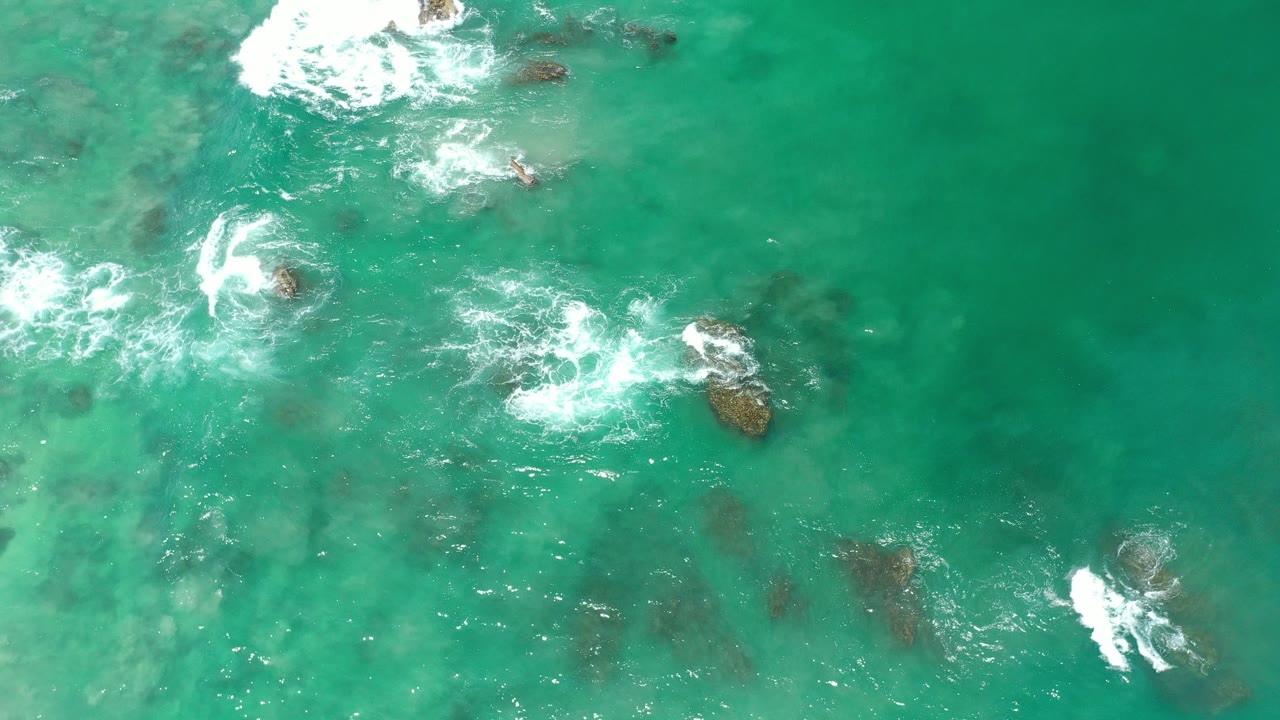Teal ocean water with white surf around scattered rocks.