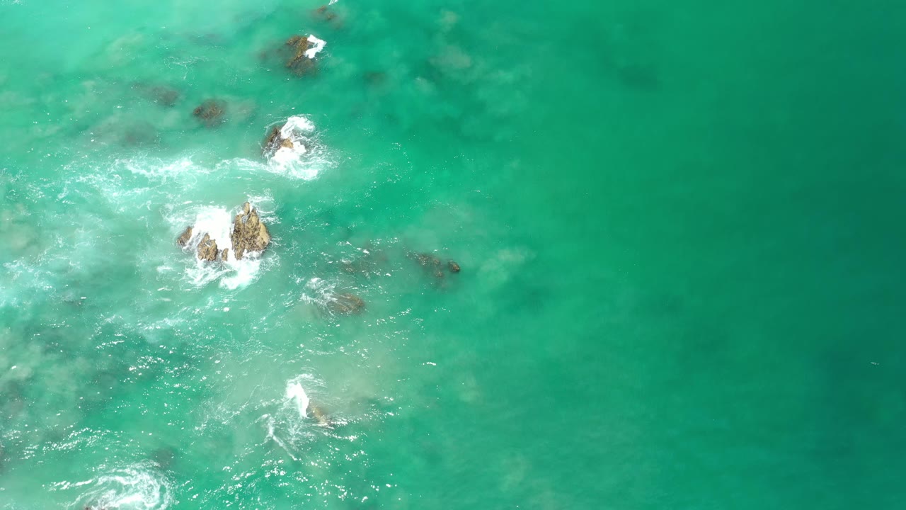 Turquoise water with rocks, foam, and open sea space.