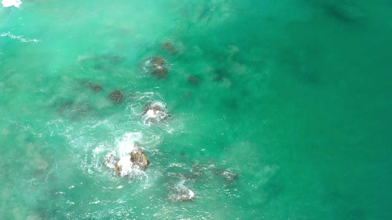 Overhead blue-green ocean water with rocks and white foam.