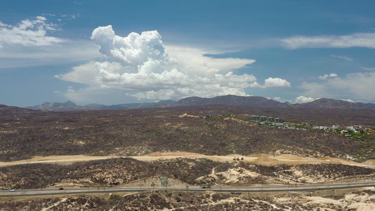 Wide aerial view of desert hills under large white clouds