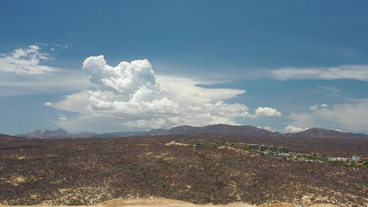 Elevated desert landscape with distant hills and large white clouds.