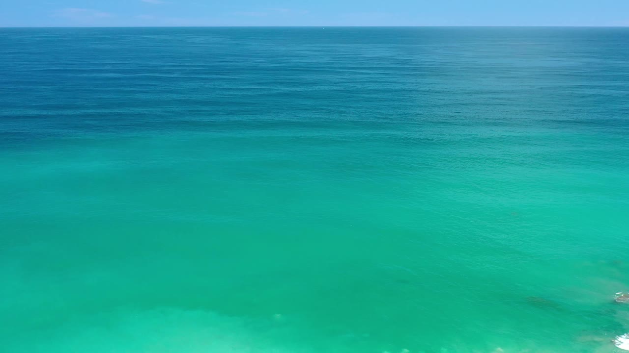 Los Cabos ocean surface one second in, showing broad turquoise water, a darker blue horizon band, faint wave lines, and no visible people.
