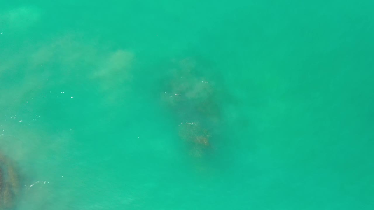 Clear green Los Cabos water fills the frame, with diffuse underwater shadows spread across the center and no visible people.