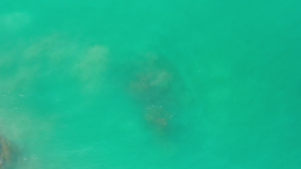 Green ocean water with darker submerged forms and light haze across the surface.