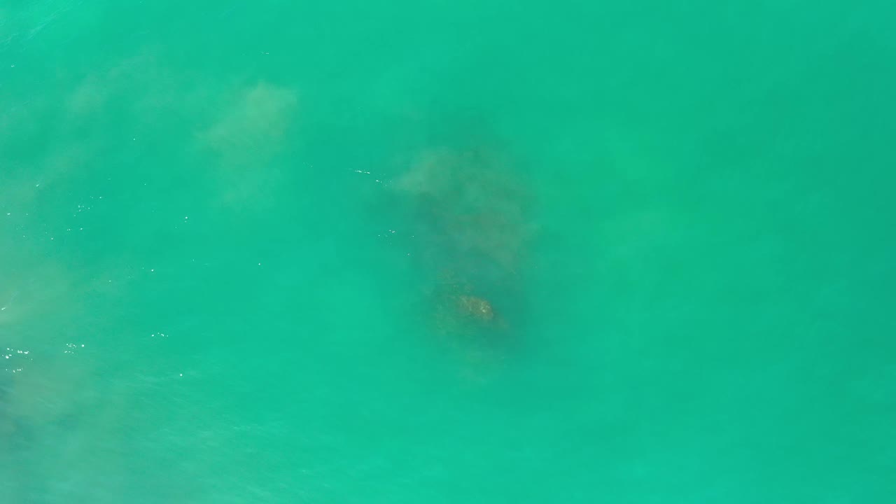 Sea-green Los Cabos water fills the frame as pale foam lines pass over a faint dark rock below the surface, with no visible people.