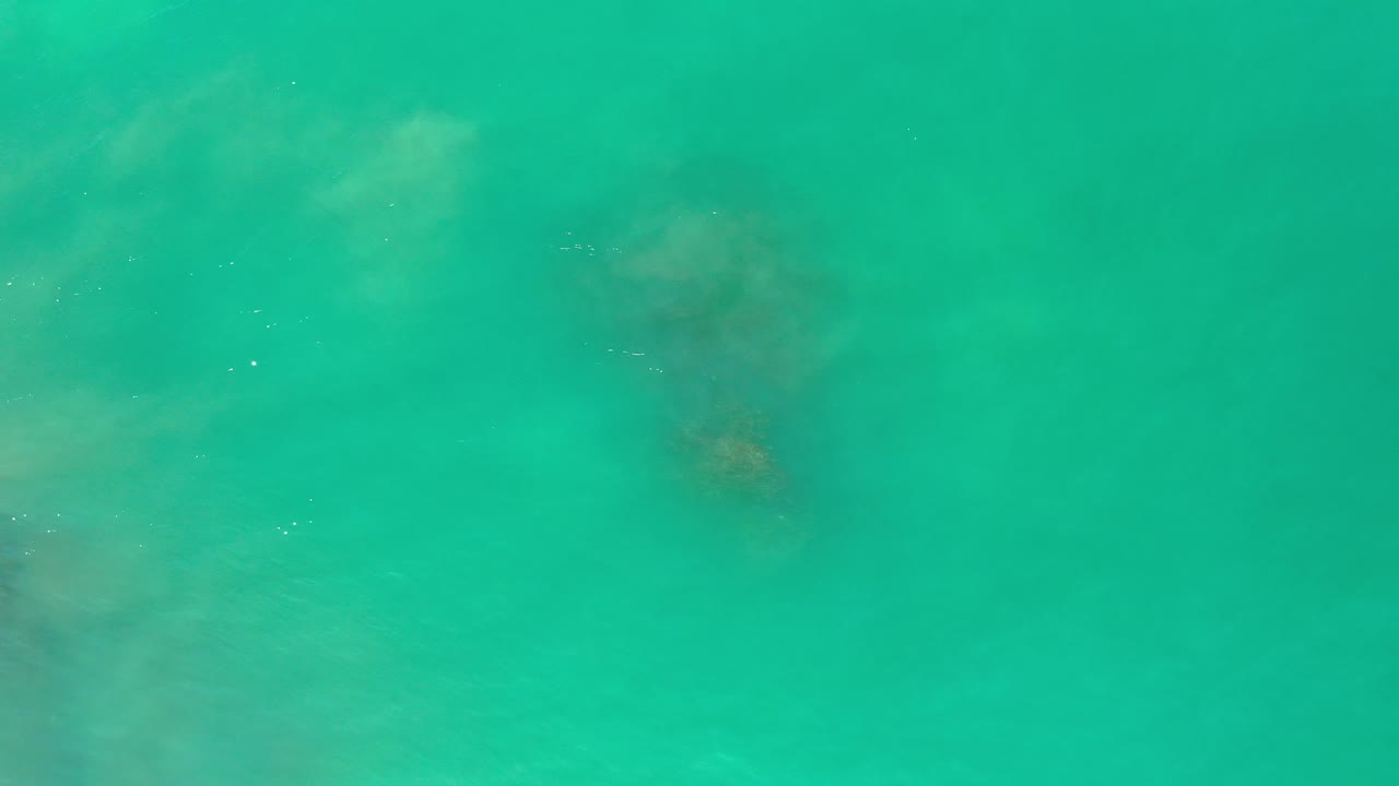 Turquoise water with a small darker rock patch near the upper area