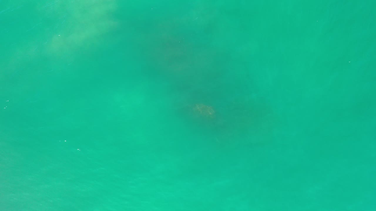 Overhead view of turquoise sea water in Los Cabos with soft dark rock shapes below the surface and no visible people.