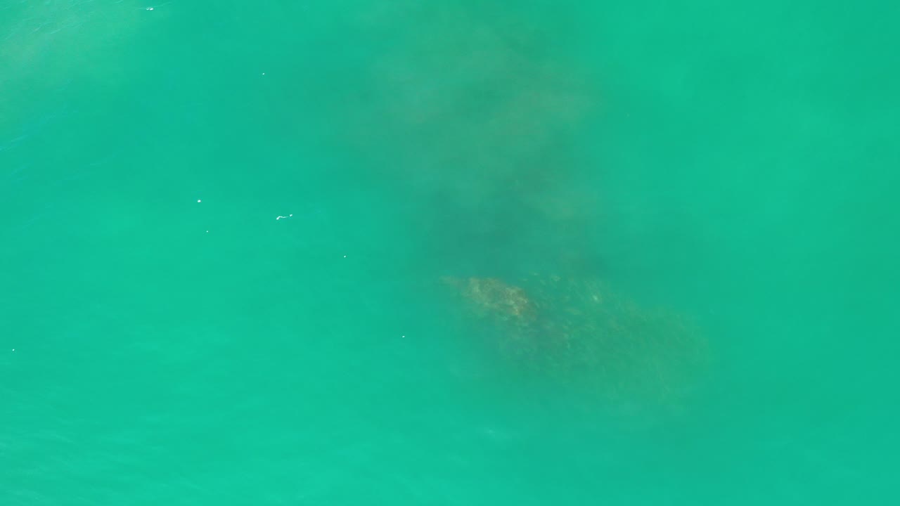 Turquoise water in Los Cabos with a faint darker submerged shape near the upper middle and no visible people.