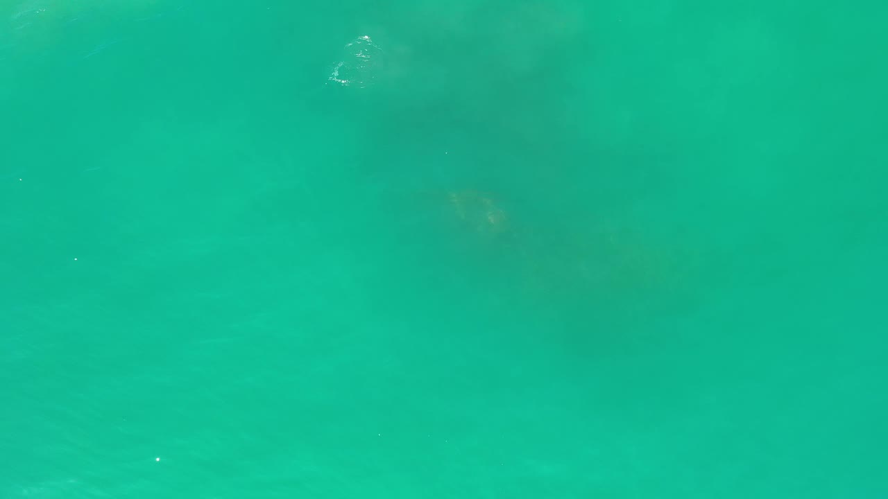 Clear blue-green ocean water in Los Cabos shows darker underwater areas near the center and lower edge, with soft surface texture and no visible people.