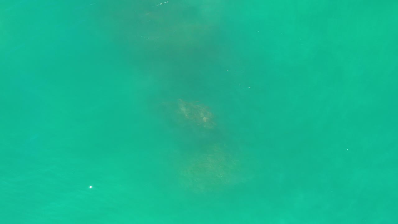 Overhead view of turquoise ocean water in Los Cabos, Mexico, with muted darker areas beneath the surface and no visible people.