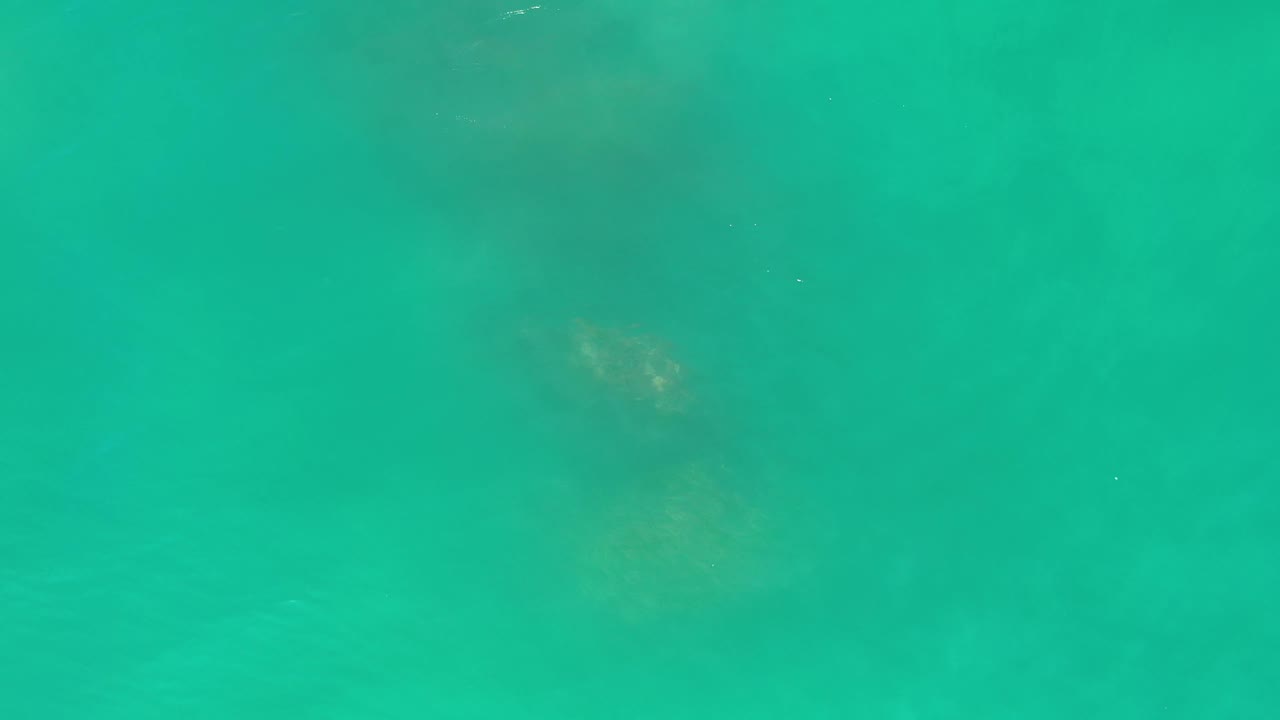 Aerial Los Cabos ocean frame with blue-green water, faint cloudy underwater texture, small bright specks, and no visible people.