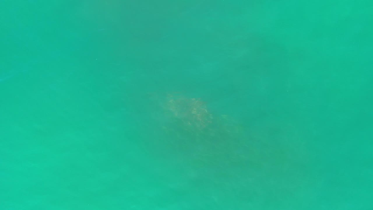 Top-down view of turquoise sea in Los Cabos, Mexico, with muted darker patches below the surface and no visible people.