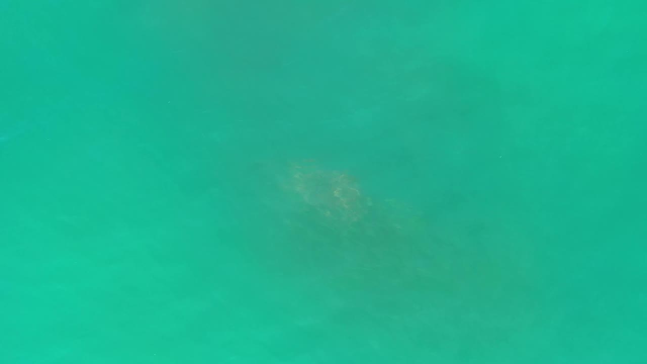 Overhead Los Cabos sea frame with blue-green water, faint mottled underwater areas, and no visible people or boats.