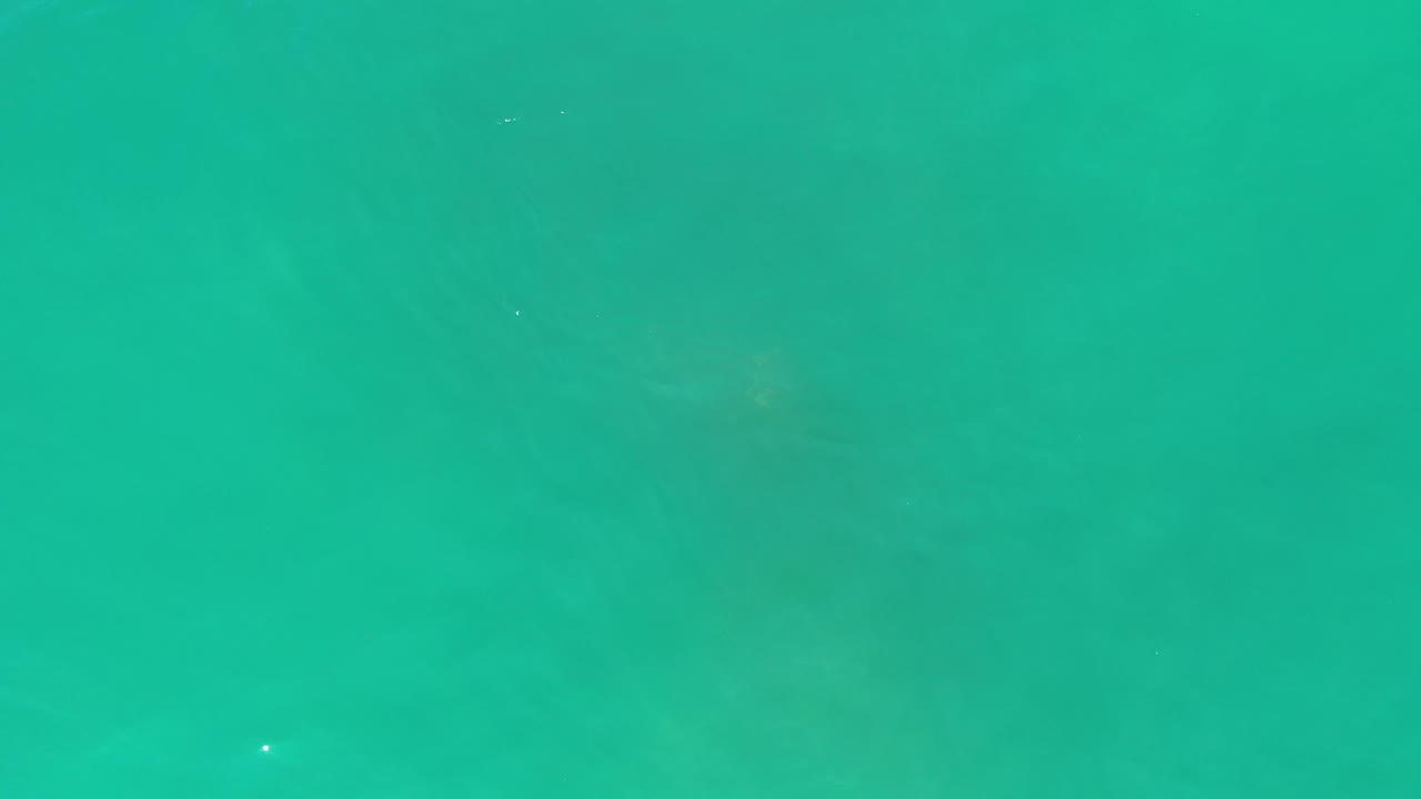 The one-second frame shows blue-green Los Cabos water with subtle ripple bands and a few tiny light specks on the surface, with no visible people.
