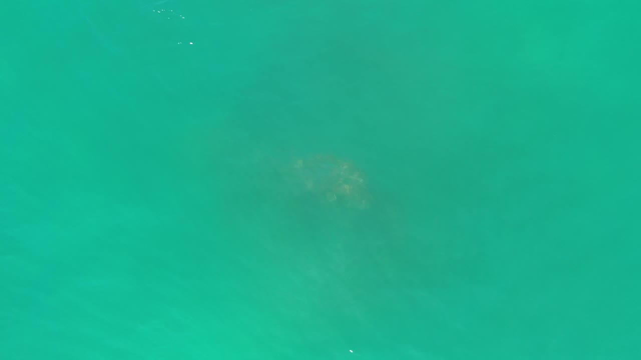 Aerial frame of clear green ocean water in Los Cabos, Mexico, with a darker underwater patch near the center and no visible people.