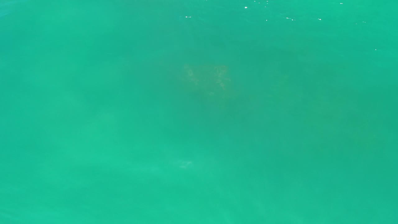 Green sea surface in Los Cabos, Mexico, with small white light glints near the upper water and no visible people or boats.
