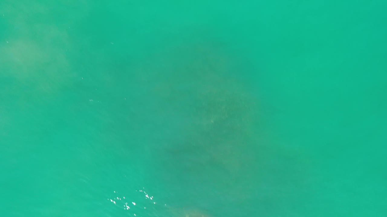 Turquoise seawater with faint underwater patches and small sun glints.