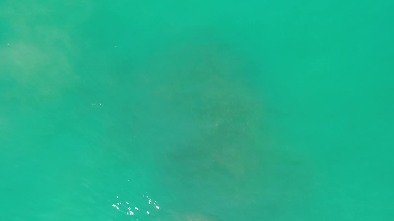 Green-blue seawater fills the frame in Los Cabos, Mexico, with a small cluster of white sun reflections near the lower left and no visible people.
