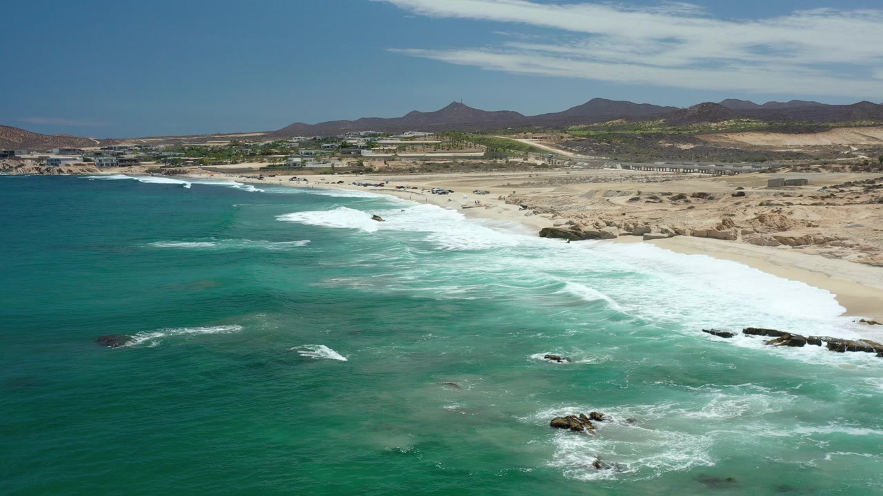 Aerial view of turquoise surf beside a sandy desert beach.