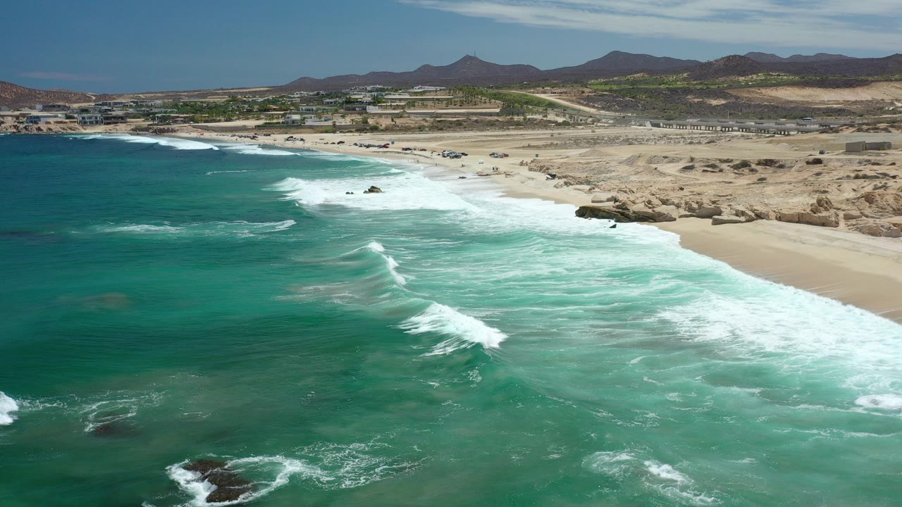 Aerial view of turquoise surf breaking along a wide empty beach.