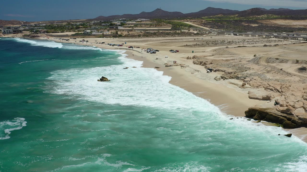 Aerial view of white waves breaking along an open sandy beach.