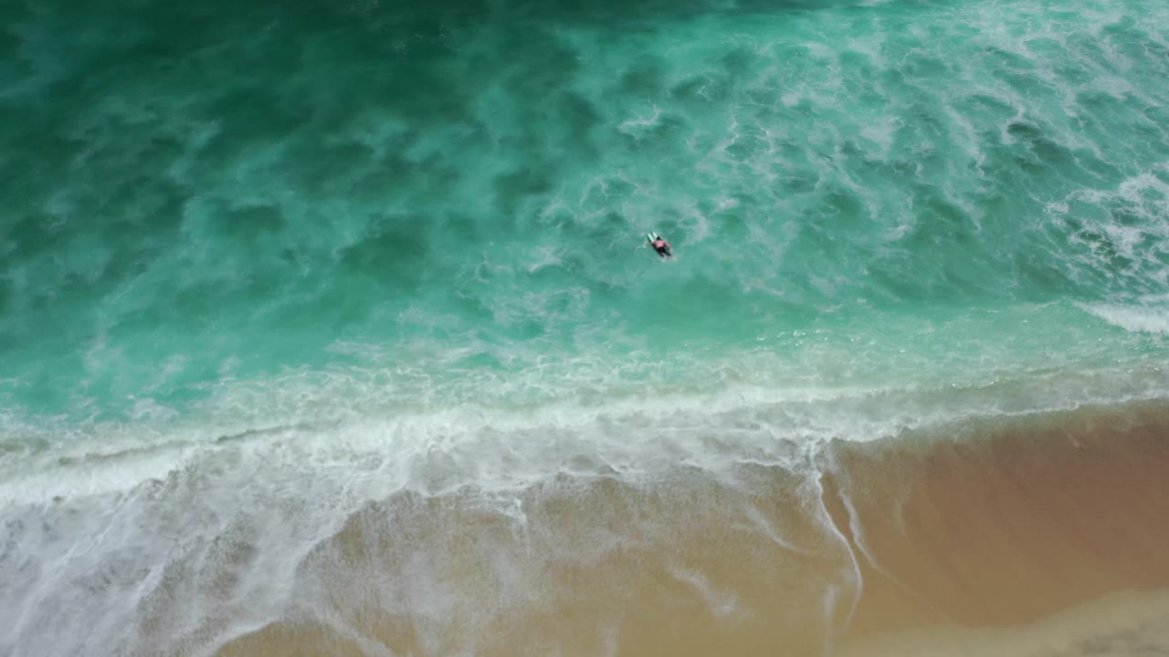 Overhead Los Cabos shoreline view with aqua water spreading into white foam over wet tan sand, with the small offshore object still visible.
