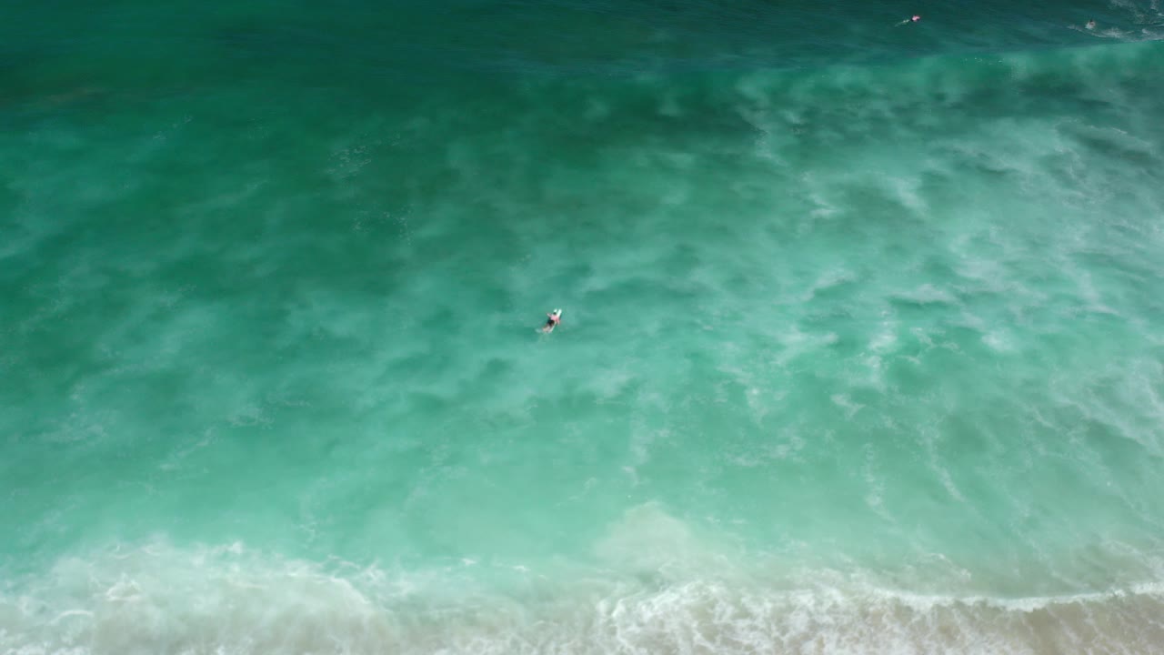 Overhead aquamarine surf with a small surfer on a board.
