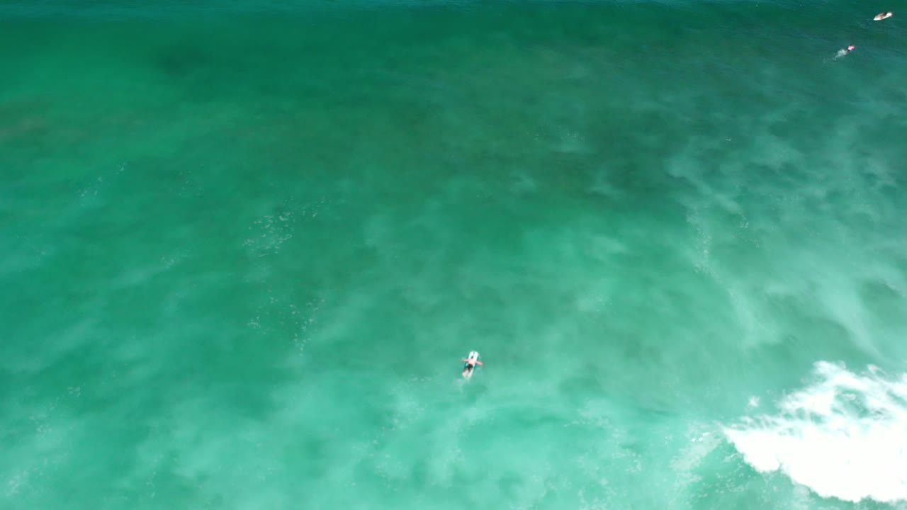 Aerial turquoise water with a small surfer near center and surf entering from the right.