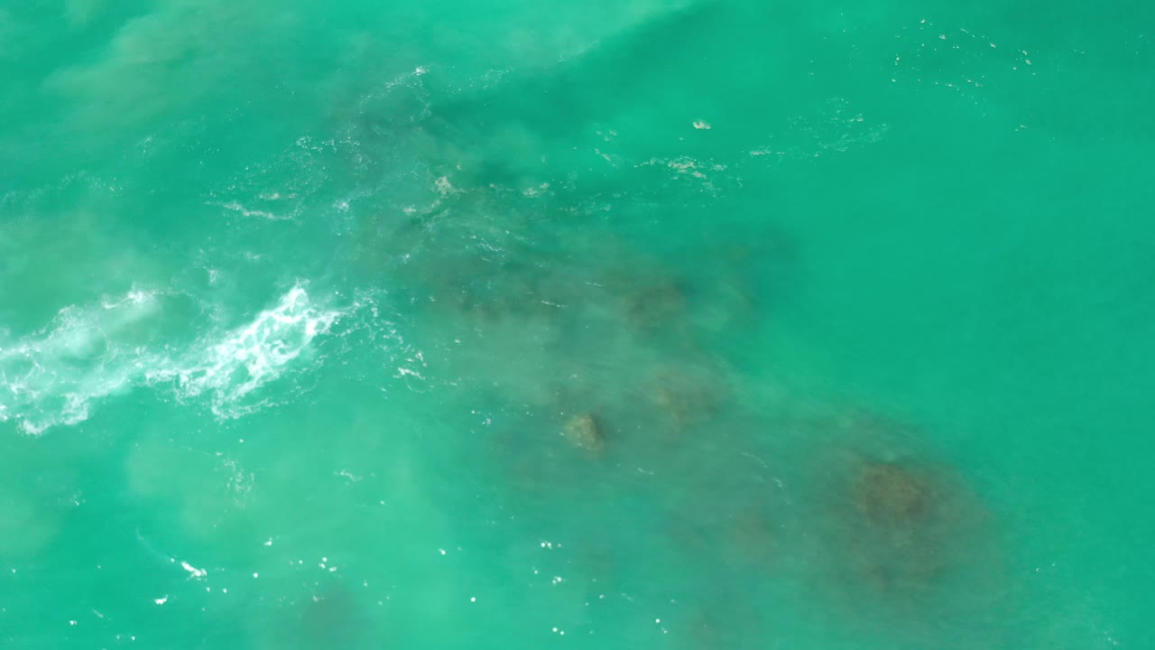 Foam line and submerged rock patches in turquoise water.