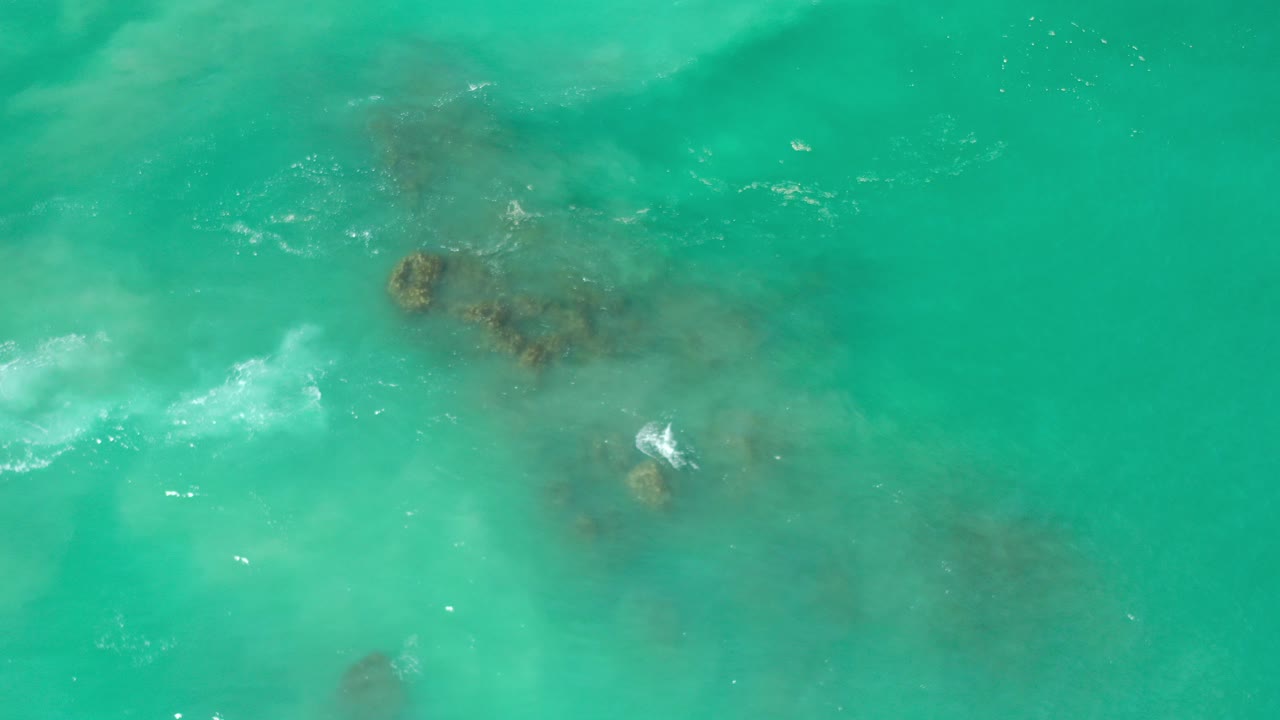 Overhead green ocean water with submerged rocks and white foam.