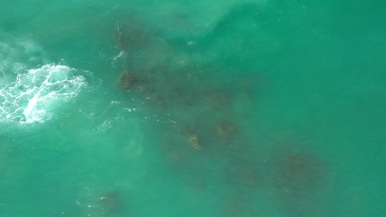 Overhead turquoise ocean with white foam and dark algae patches.