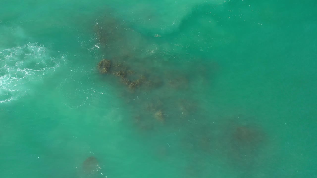 Turquoise water with darker reef shapes and a small foam break.