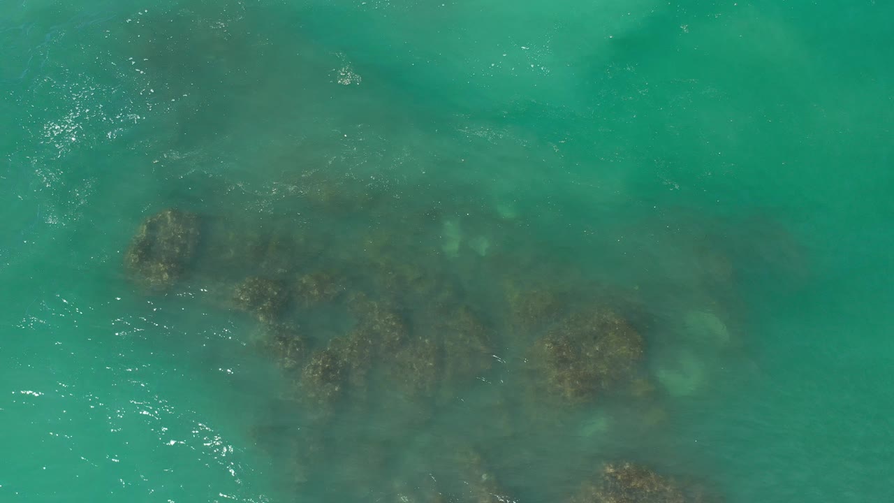 Overhead view of clear green ocean water over dark submerged rocks in Los Cabos, Mexico, with small surface highlights and no visible people.