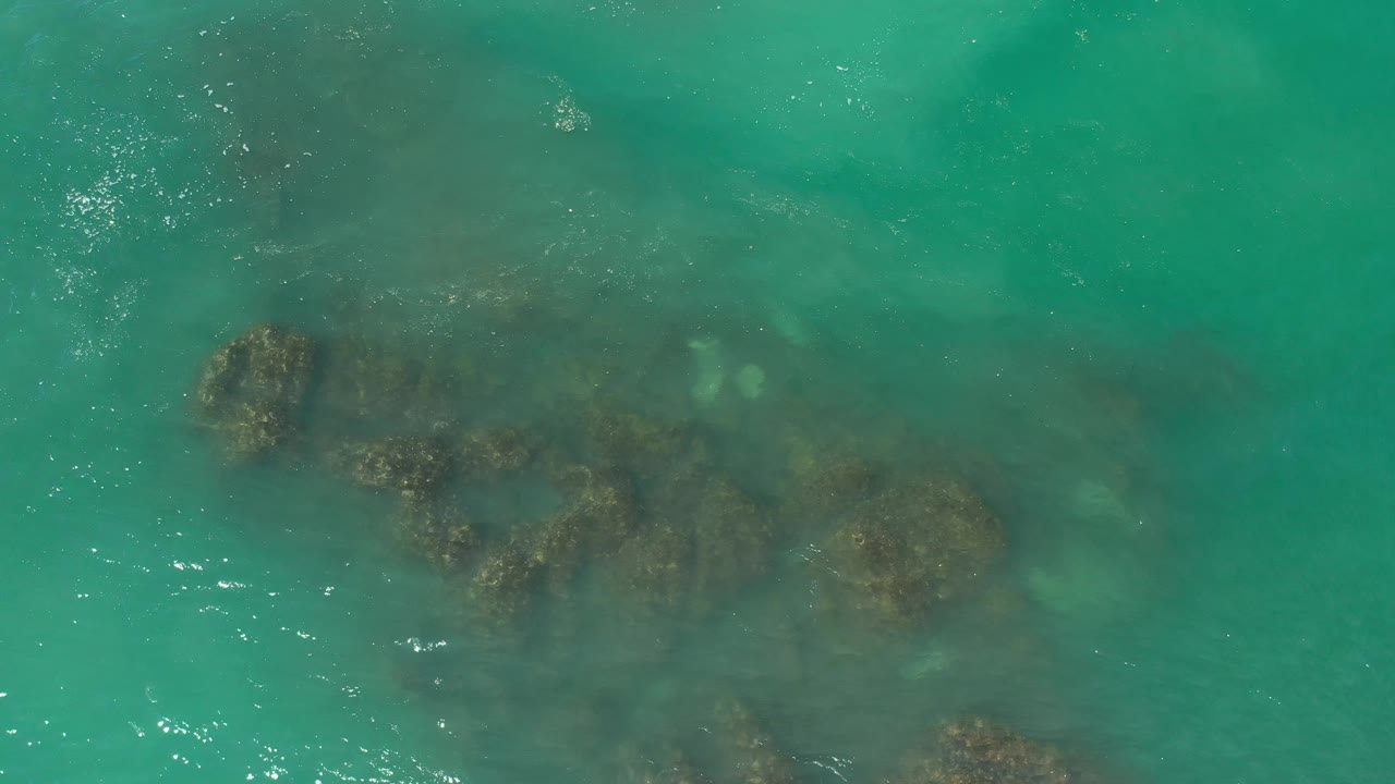 Clear ocean surface above dark coastal rocks.