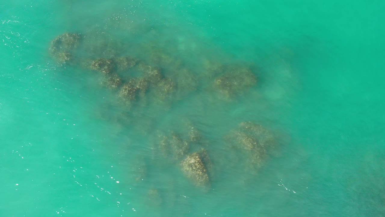 Aerial-style sea surface with scattered submerged rocks.