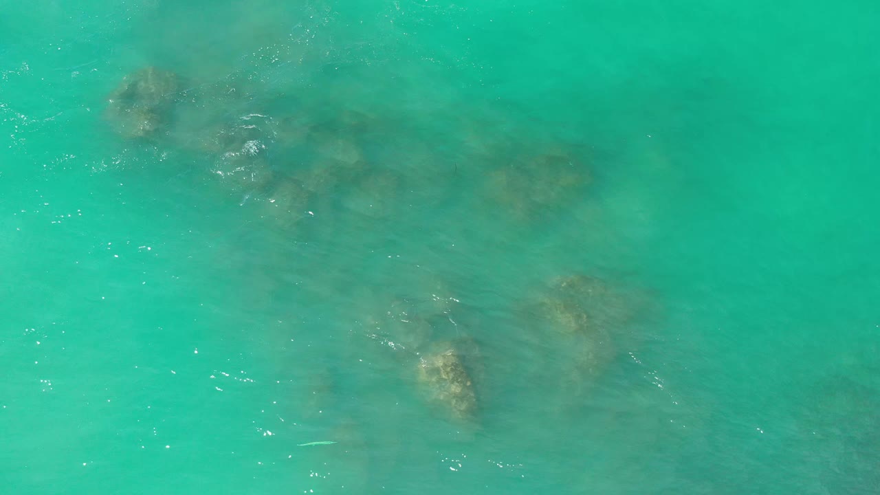 Blue-green ocean water fills the frame in Los Cabos, Mexico, with darker reef shapes under the surface and faint wave sparkle crossing the center, no visible people.